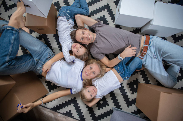 Image from above of women, men and children lying on floor among cardboard boxes - 写真・画像
