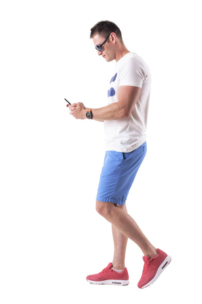 Oldalnézetből fiatalember nyári ruhák gyalogos- és a mobiltelefon. Teljes test elszigetelt fehér background.  - Fotó, kép