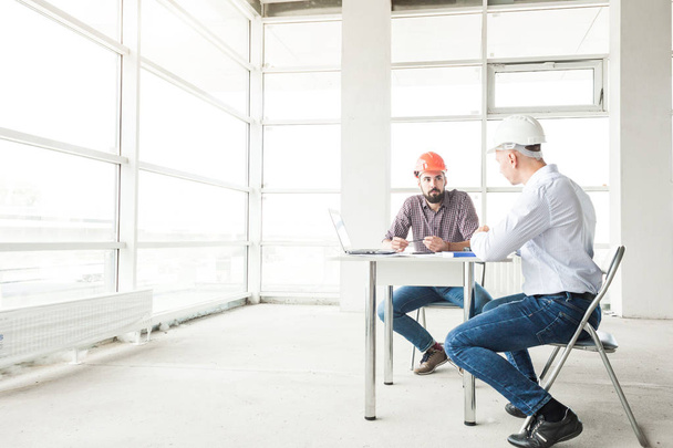 male engineers, architects working at the desk in helmets. Drawings, laptop, roulette on the desktop. Reception and supervision of building construction - Photo, Image