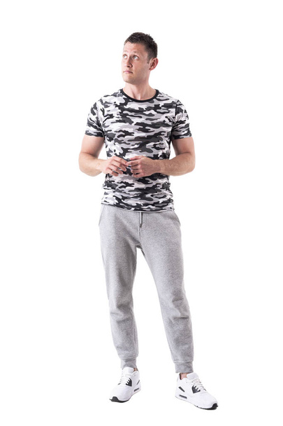 Hombre joven adulto con ropa deportiva y camiseta del ejército mirando hacia arriba y pensando. Cuerpo completo aislado sobre fondo blanco
.  - Foto, Imagen