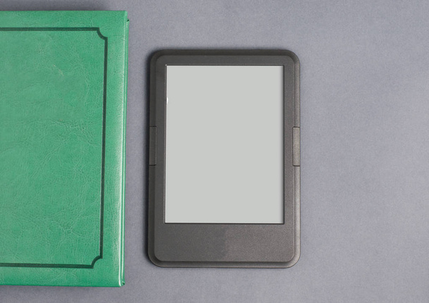 E-book reader and the green book. Gray background. Flat top view. Space for tex - Photo, image