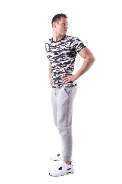 Handsome athletic man in sweatpants and camo shirt looking back over the shoulder. Full body isolated on white background.  - Фото, изображение