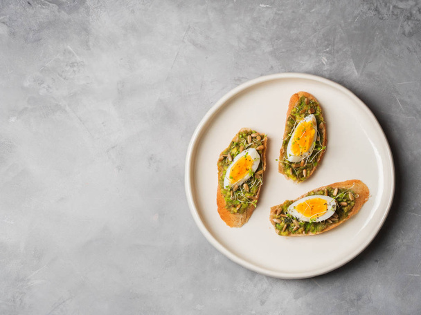 Whole-grain toasts plated avocado with eggs on ceramic white plate over grey concrete background, top view, Diet food concept, gluten-free   - 写真・画像