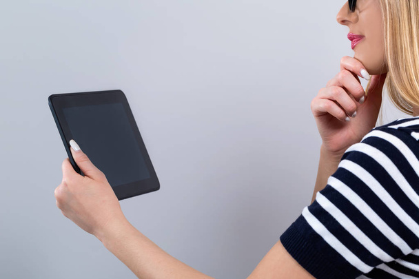 Young woman with a tablet computer on a gray background - Fotoğraf, Görsel