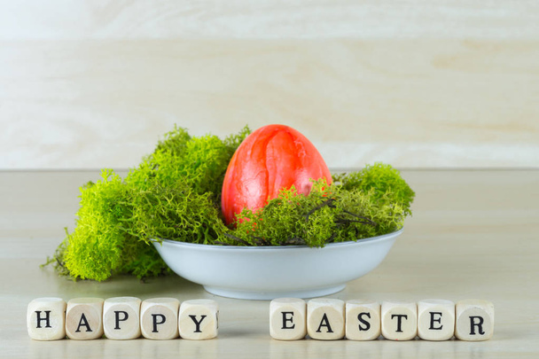 Una pequeña canasta de Pascua con musgo y un huevo de Pascua rojo, antes de que las palabras feliz Pascua
 - Foto, Imagen