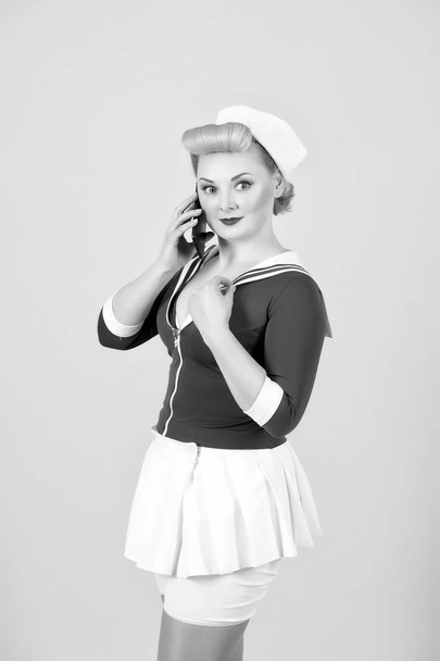 Sailor dressed girl with smart-phone isolated on pink background. Blond girl with curls and pin-up make-up talking over cellular - Φωτογραφία, εικόνα