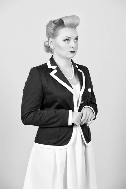 Serious blonde girl in jacket looks up. Woman in pin-up style dreaming standing in studio with closed hands. Blond female with styled make-up - Фото, зображення