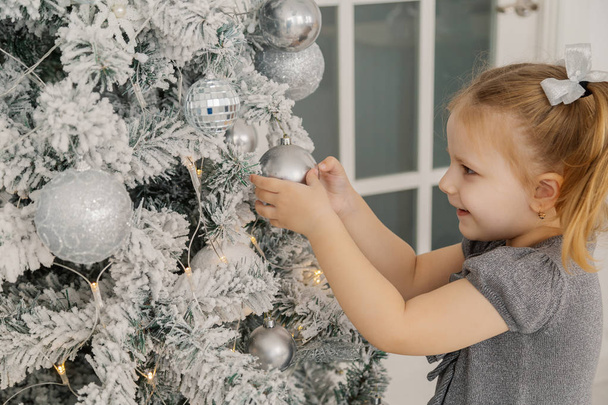 Uma menina está ao lado de uma árvore de Natal e tocando brinquedos
 - Foto, Imagem