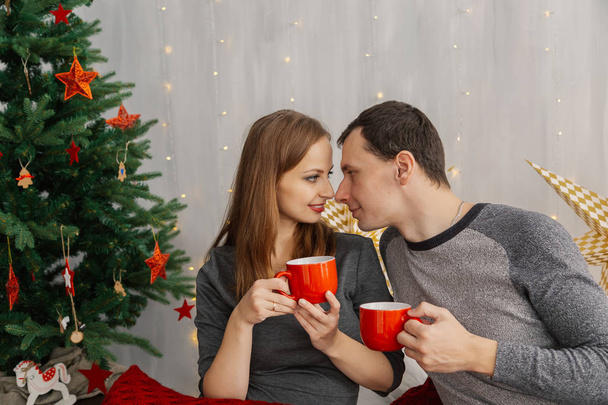Family couple on the bed in the New Years room holding red mugs with tea. - Photo, Image