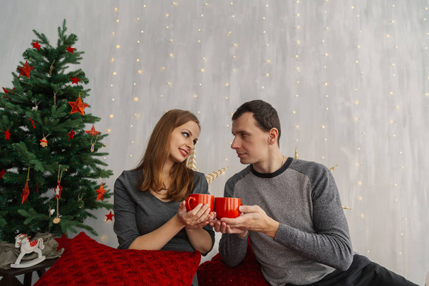 Family couple on the bed in the New Years room holding red mugs with tea. - Fotoğraf, Görsel