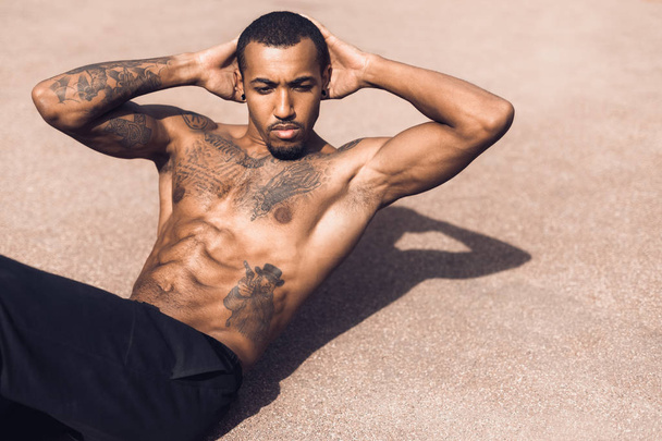 African-american man exercising sit ups on sports ground - Photo, Image