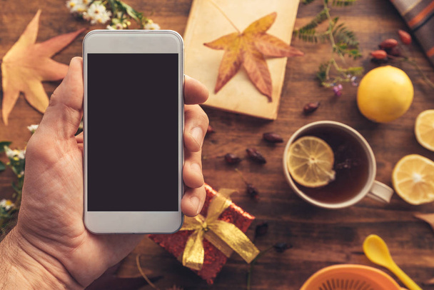 Smartphone in hand mock up with autumn season decoration, overhead view of mobile phone with blank screen - Foto, Imagem
