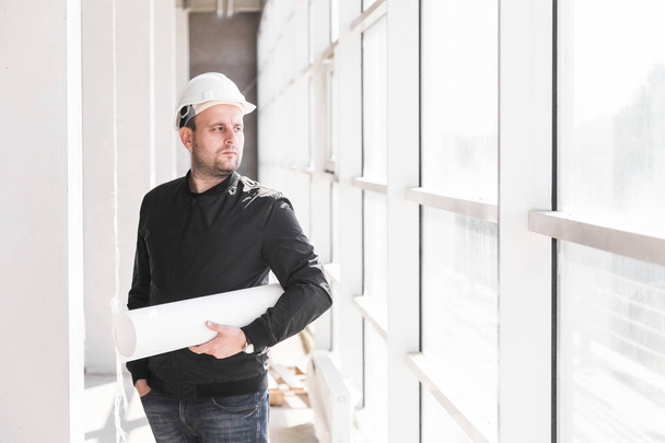 the builder architect in a helmet with drawings is working at the construction site. supervision of construction. bargain, apartment purchase, real estate - Foto, Imagen