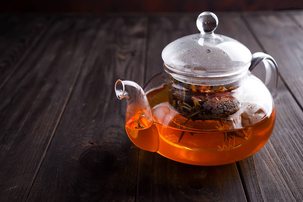 Glass teapot with freshly brewed herbal tea bound on a wooden brown background with space for text. - Photo, image