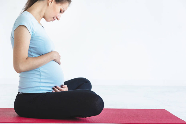 pregnancy, sport, fitness, people and healthy lifestyle concept - happy pregnant woman exercising yoga and and meditating in lotus pose in white background gym - Foto, imagen