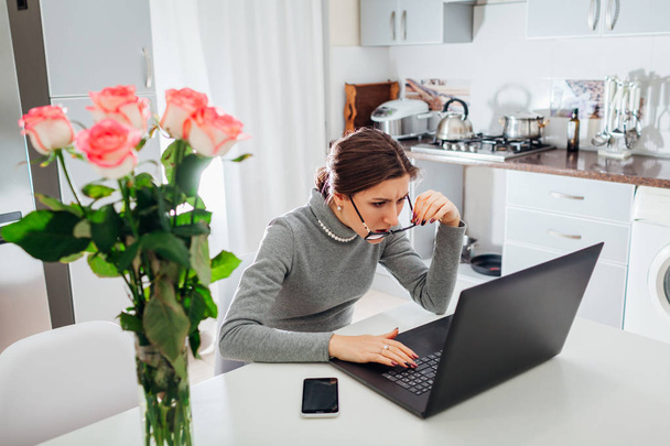 Femme parlant de travail sur ordinateur portable sur la cuisine moderne. Colère irritée pigiste regardant l'écran enlever les lunettes
 - Photo, image