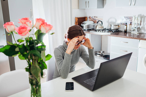 Woman working on laptop on modern kitchen. Young tired freelancer having headache. Lady upset - Фото, изображение