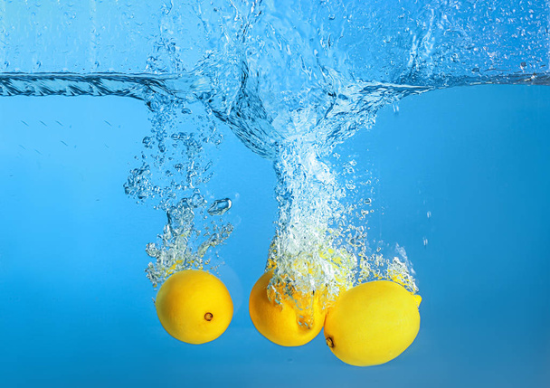 Fallen von Zitronen ins Wasser auf farbigem Hintergrund - Foto, Bild