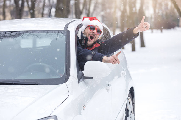 Portrait of car driver with santa hat through car window. On the road winter vacation and holidays concept. - Fotó, kép