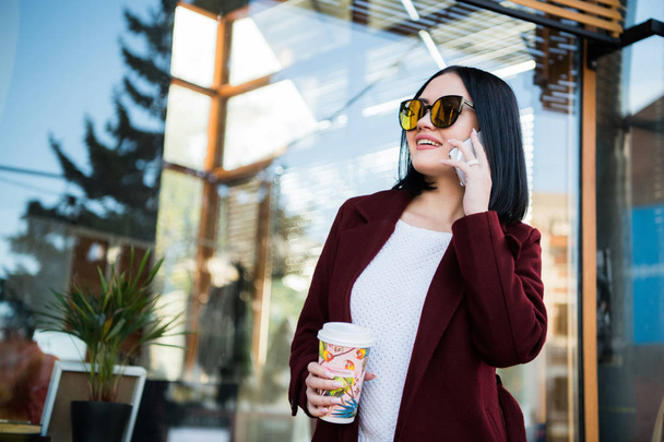 Ritratto di giovane donna che tiene il caffè per andare a parlare al telefono
 - Foto, immagini