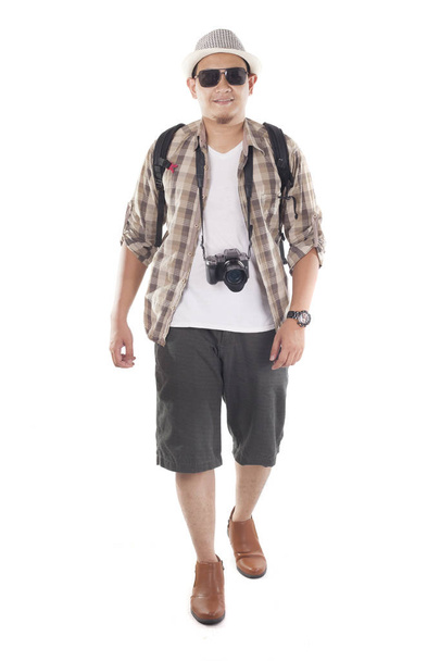 Traveling people concept. Portrait of Asian male backpacker tourist wearing hat, black sunglasses, camera and backpack isolated on white. Full body portrait. Smiling happy gesture - Photo, Image