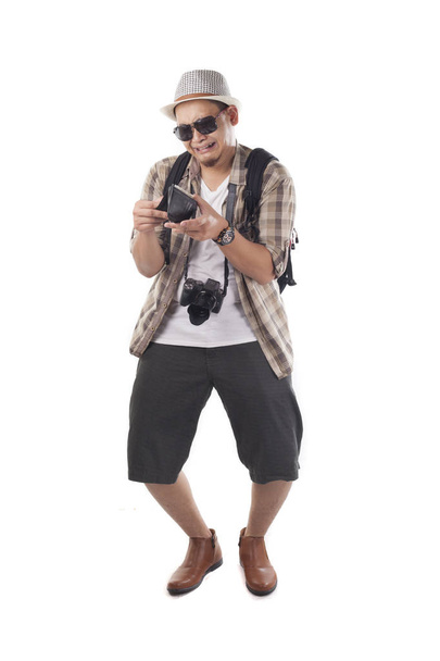 Traveling people concept. Portrait of Asian male backpacker tourist wearing hat, black sunglasses, camera and backpack isolated on white. Full body portrait. Broke empty wallet - 写真・画像