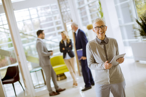Portrait de femme d'affaires senior debout avec tablette numérique tandis que d'autres hommes d'affaires debout en arrière-plan
 - Photo, image