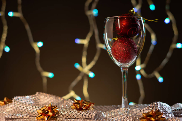 Christmas cards. Wine glass with red, blue and gold Christmas decorations on dark background with christmas tree garland. - Valokuva, kuva