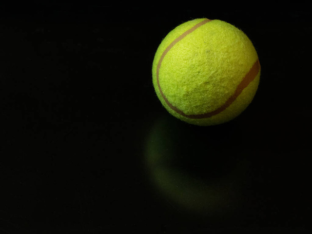 one yellow green tennis ball on dark glossy surface background. first place gold winner at Wimbledon Championship concept - Fotoğraf, Görsel