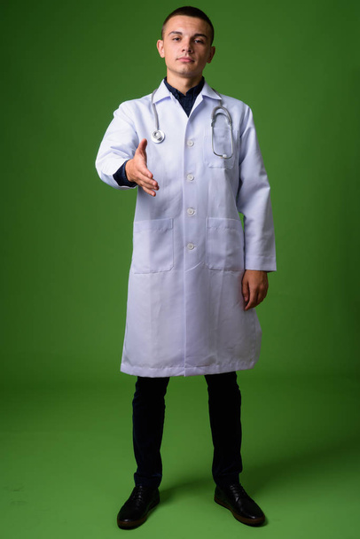 Young handsome man doctor against green background - Fotó, kép
