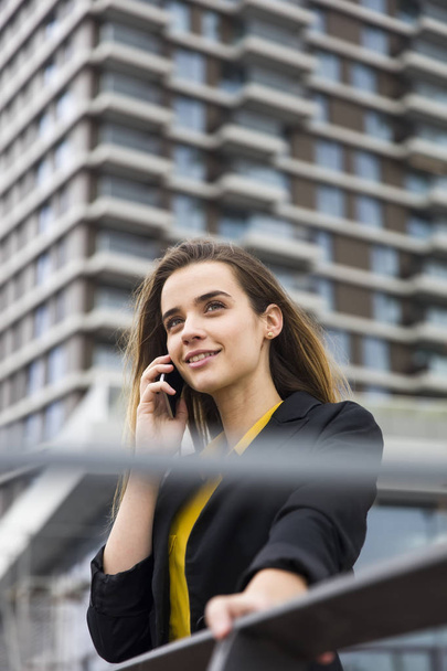 Молодая деловая женщина использует мобильный телефон на улице против офисного здания
 - Фото, изображение