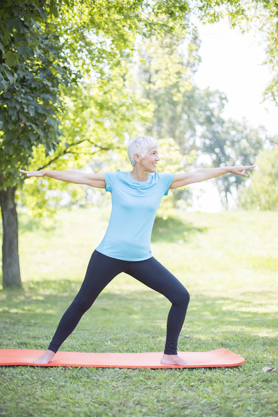 Senior dames lichaam flexibiliteit verbeteren door strekken in het park - Foto, afbeelding