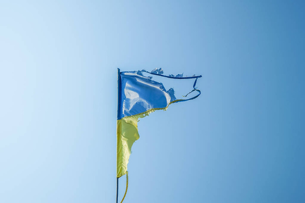 потрепанный украинский флаг, развевающийся на ветру против голубого неба
 - Фото, изображение