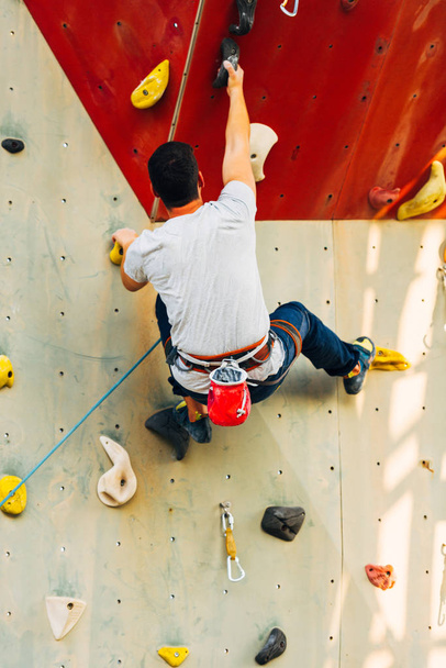 Νεαρός ορειβάτης σκαρφαλώνει σε πρακτικό βράχο στο αναρριχητικό κέντρο, πετώντας - Φωτογραφία, εικόνα