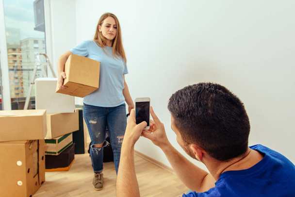 Guy picture his girlfriend while holding cardboard box in living room - Foto, immagini