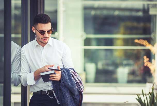 Σύγχρονη νεαρός επιχειρηματίας κρατώντας σημειωματάριο ακούγοντας μουσική στα ακουστικά - Φωτογραφία, εικόνα