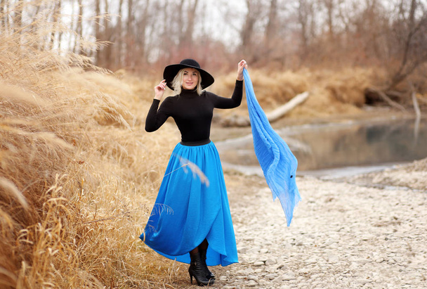 Vista completa de la mujer rubia en sombrero posando al aire libre por río
 - Foto, imagen