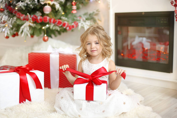 girl and a gift sitting near the Christmas tree - Fotó, kép