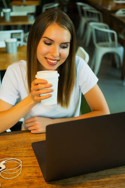 Felice giovane donna bionda che beve caffè o tè e utilizza il computer portatile in una caffetteria
 - Foto, immagini