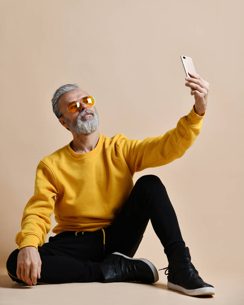 Portrait of happy senior millionaire man using smartphone cellphone make selfie in yellow sunglasses - Φωτογραφία, εικόνα