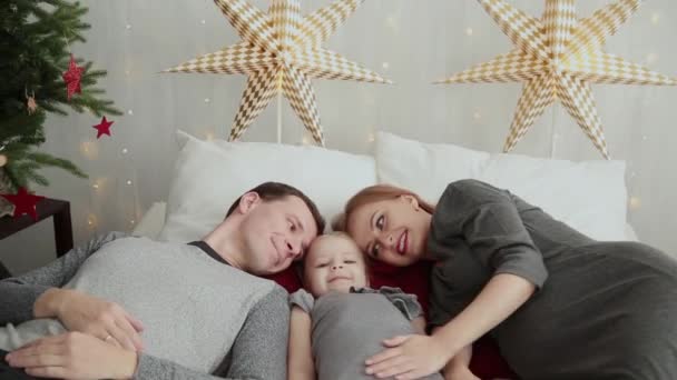 クリスマスの朝。若い家族は喜んでお互いを果たしています。たくさんの枕、明るい包装やクリスマスの飾りでクリスマス プレゼントのベッド。メリー クリスマス 2019. - 映像、動画