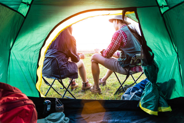 Male and female campers talking each others in front of camping tent. People and lifestyles concept. Picnic and travel concept. Nature in summer theme. Back view and inside of tent angle - 写真・画像
