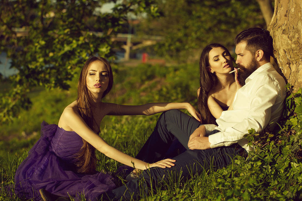 Бородатый мужчина и две женщины на траве
 - Фото, изображение