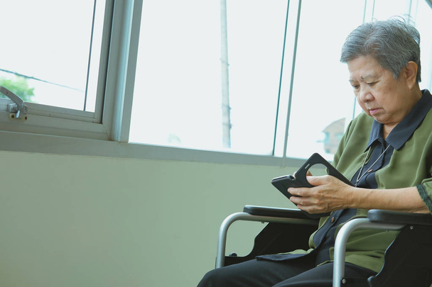 Starší žena na vozíku drží mobilní telefon. starší ženské SMS zpráv, pomocí aplikace s mobil. Asijské starší smartfon pro on-line sociální síťové připojení - Fotografie, Obrázek