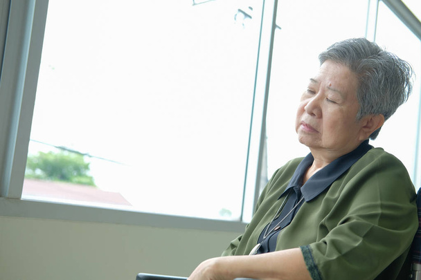 tylsistynyt aasialainen vanhempi nainen pyörätuolissa nukkumassa lähellä ikkunaa. iäkäs nainen väsymys uupunut. vanhempi vapaa-ajan elämäntapa
 - Valokuva, kuva
