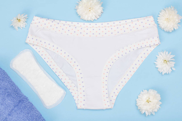 Beautiful panties with sanitary napkin, towel and flower buds on blue background. Women underwear set. Top view. - Photo, Image