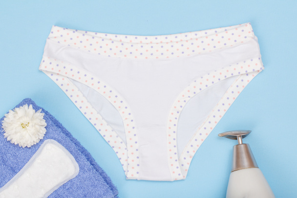 Beautiful panties with towel, sanitary napkin and bottle with liquid soap on blue background. Women underwear set. Top view. - Photo, Image