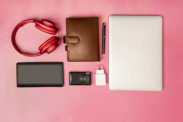top view of laptop, pen, notebook, camera, wallet and headphones for work on pink background. View from above - Foto, Bild