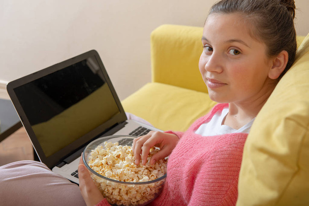 adolescente sonriente usando una computadora portátil y comiendo palomitas de maíz
 - Foto, imagen
