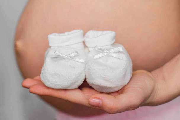 manos de una mujer embarazada con botines para un recién nacido
 - Foto, imagen